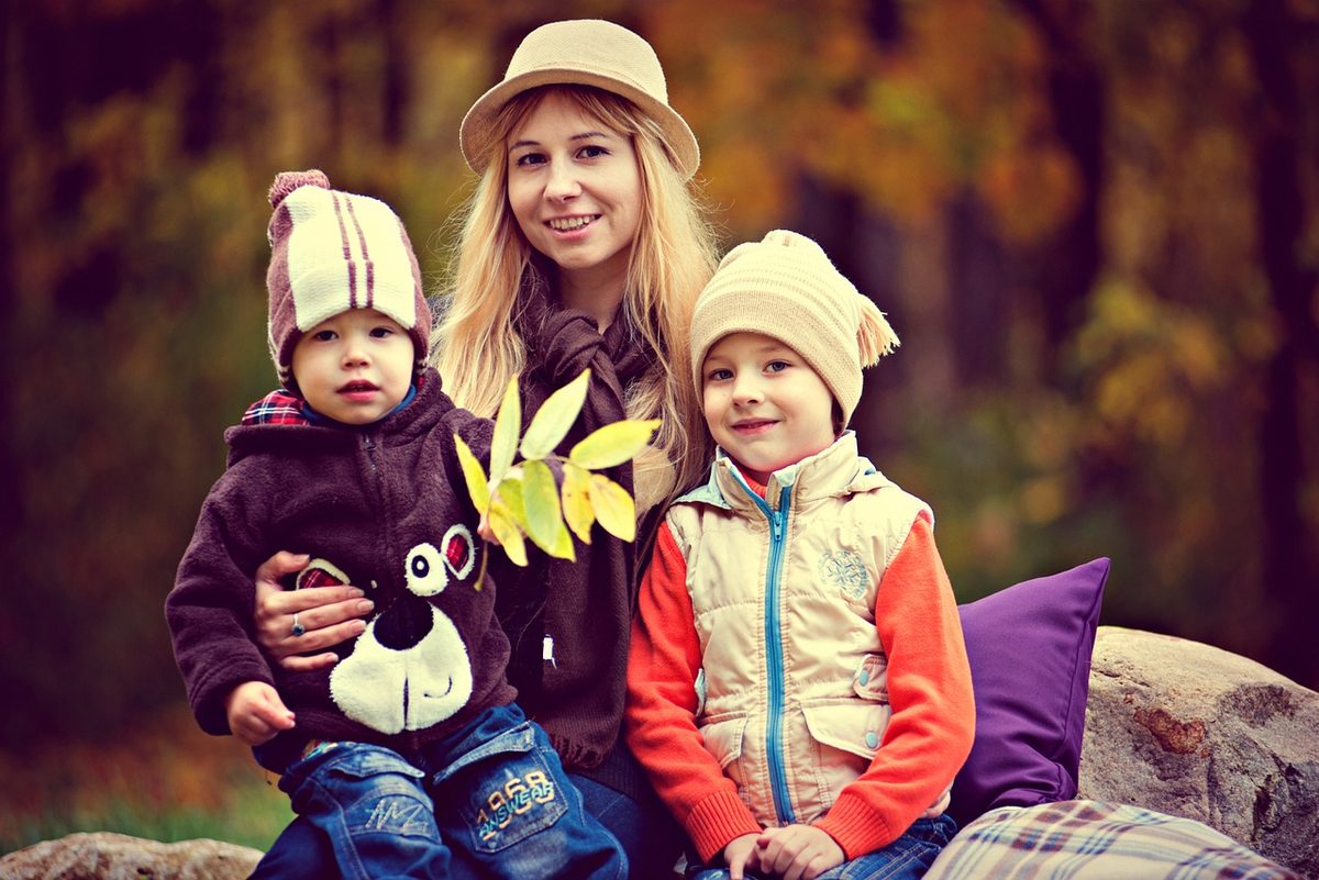 A mother sitting outdoors in the fall with her two young children in winter hats